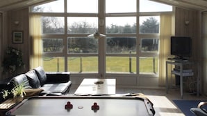 A room with a pool table, a sofa, and large windows offering a view of the outdoors.