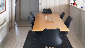 A dining area with a wooden table and black chairs, a white vase on the table, and a framed picture on the wall.