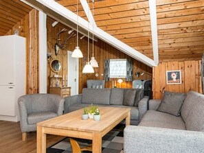 A cozy cabin interior with a wooden ceiling, a sofa set, a wooden coffee table, and a dining table.
