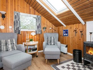 A cozy room with wooden walls, a skylight, a fireplace, and two grey sofas with patterned cushions.