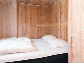 A single bed with white bedding in a room with wooden walls and a door.