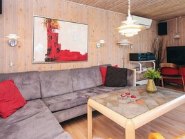 Una sala de estar moderna con un sofá gris, cojines rojos, una mesa de centro con objetos decorativos y un cuadro abstracto grande en la pared.