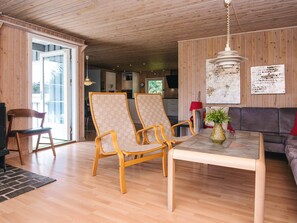 A spacious living area with wooden flooring, a dining table, two chairs, a sofa, and a hanging light fixture.