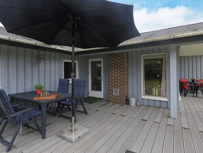 Ein überdachter Patio-Bereich mit Tisch und Stühlen, einem großen Sonnenschirm und einer Ziegelstütze.