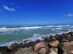 A rocky shoreline with waves crashing against the rocks under a clear blue sky.