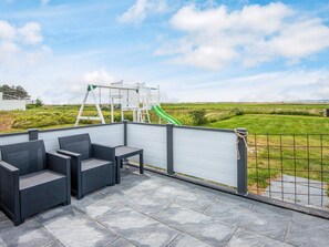 A patio with outdoor furniture, a playground, and a view of the countryside.