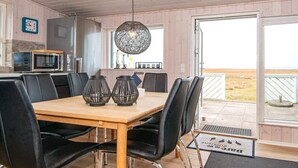 A dining area with a wooden table, black chairs, a hanging light fixture, and a view of the beach through a glass door. - 5 Star Holiday Home in Ebeltoft (Ebeltoft)