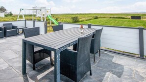 An outdoor patio with a table and chairs, a children's play structure, and a view of the countryside. - 5 Star Holiday Home in Ebeltoft (Ebeltoft)