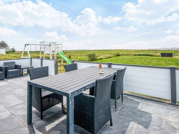An outdoor patio with a table and chairs, a children's play structure, and a view of the countryside.