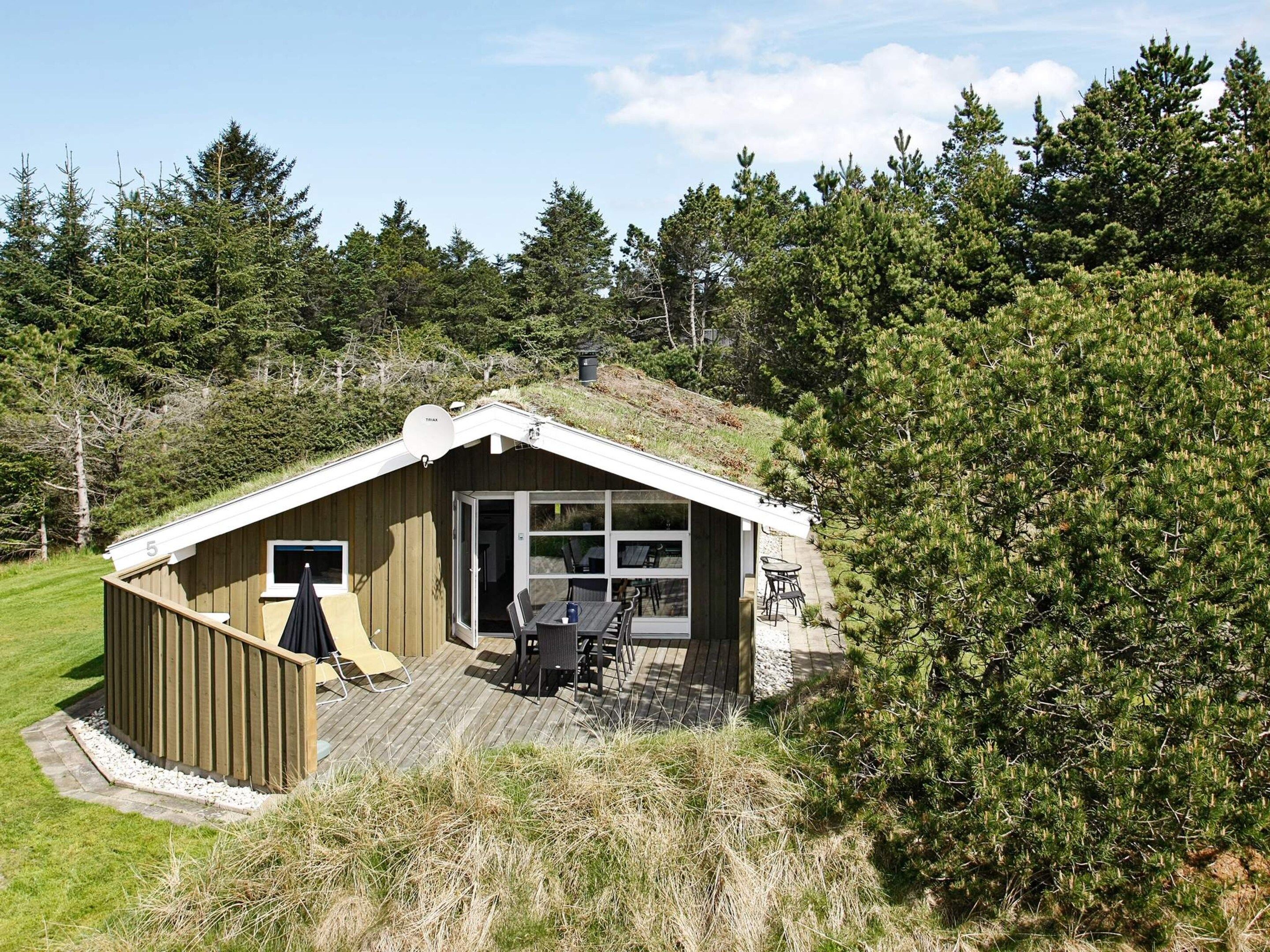 A small wooden cabin with a sloped roof, a deck, and a glass door leading to an outdoor seating area.