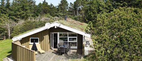 A small wooden cabin with a sloped roof, a deck, and a glass door leading to an outdoor seating area.