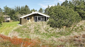 A small cabin with a sloped roof, surrounded by dense forest and grassy terrain.