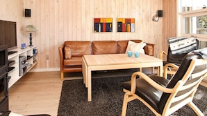 A cozy room with a wooden ceiling and walls, a brown leather sofa, a wooden table, and a black leather chair.