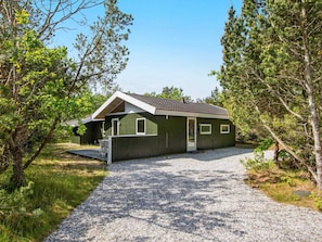 A single-story building with a gravel driveway, surrounded by trees.