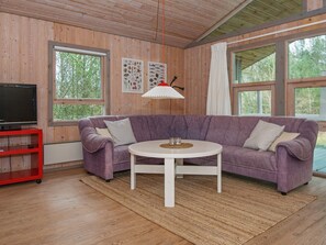 A room with a purple sofa, a white table, a red TV stand, and a large window with a view of trees.