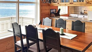 A wooden dining table with six chairs, a chandelier, and a view of the water through large windows. - 4 Star Holiday Home in Leikanger (Sogndal)