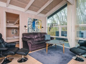A modern living room with a leather sofa, two black chairs, a small table, and a large window offering a view of trees. - 5 Star Holiday Home in Ebeltoft (Ebeltoft)