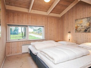 A bedroom with wooden panel walls, a large window, a bed with white bedding, and a painting on the wall. - 5 Star Holiday Home in Ebeltoft (Ebeltoft)