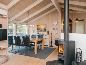 A modern interior with a dining area, wooden walls, a fireplace, and a large window. - 5 Star Holiday Home in Ebeltoft (Ebeltoft)