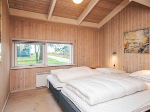 Une chambre avec des murs lambrés en bois, une grande fenêtre, un lit avec une literie blanche et un tableau accroché au mur.