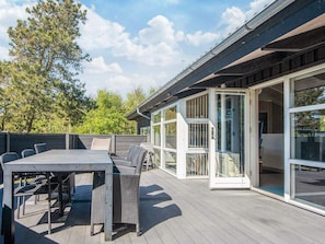 Une terrasse extérieure avec une table et des chaises, une porte vitrée donnant sur une pièce et une vue sur les arbres.