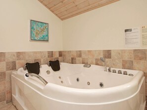 A large, white, freestanding bathtub with multiple faucets and control knobs, set against a tiled wall with a wooden ceiling.