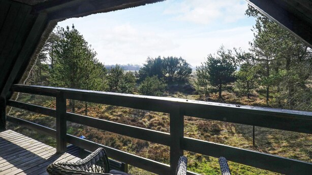 A wooden deck with wicker chairs, overlooking a forested landscape.
