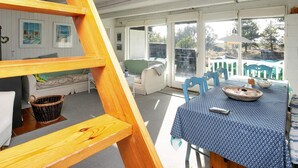 A cozy room with a wooden ladder, a dining table with chairs, a sofa, and a view of the outdoors through a glass door.