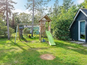 A playground with swings and a slide, a wooden playhouse, and a small shed.