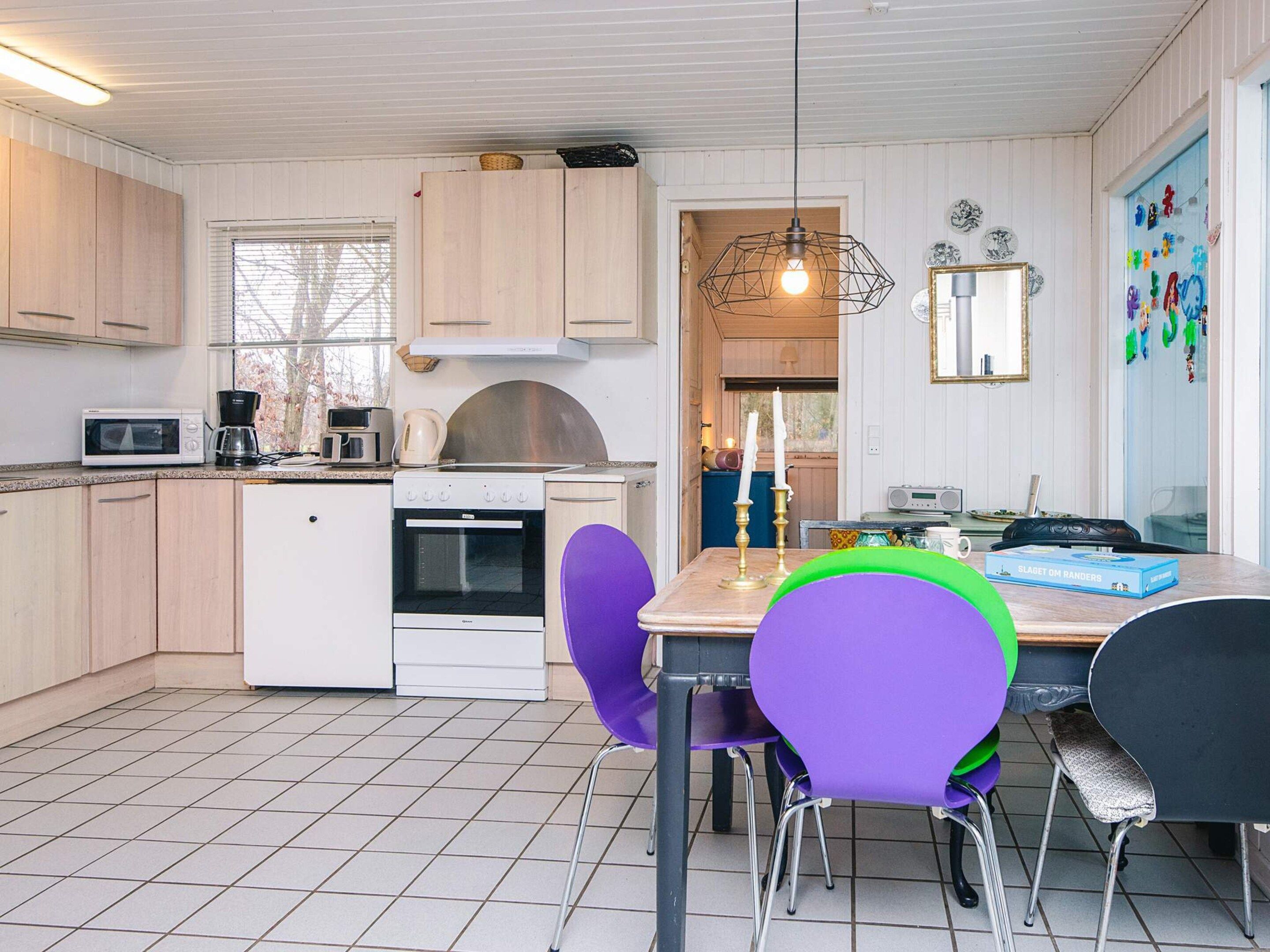 A compact kitchen with a microwave, coffee maker, oven, and a small refrigerator. There is a dining table with purple chairs and a candle.