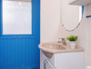 Une salle de bain avec une porte bleue, un lavabo agrémenté d’une plante et un porte-serviettes.