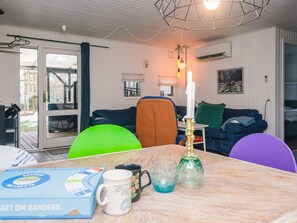 A cozy living room with a dining table, chairs, and a couch. There is a window with curtains, a painting on the wall, and a ceiling light fixture. - 8 Person Holiday Home in Orsted (Ørsted)