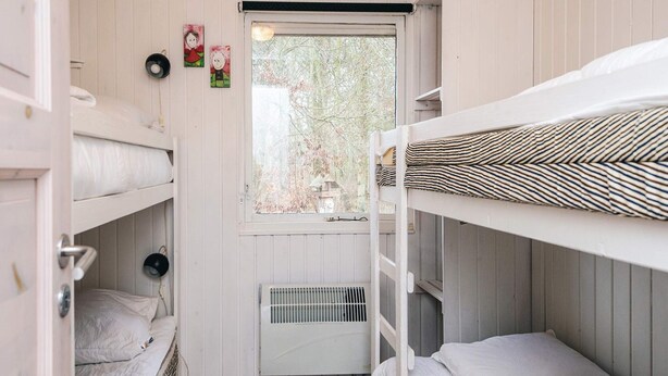 A dormitory room with bunk beds, a window with a view of trees, and a radiator.