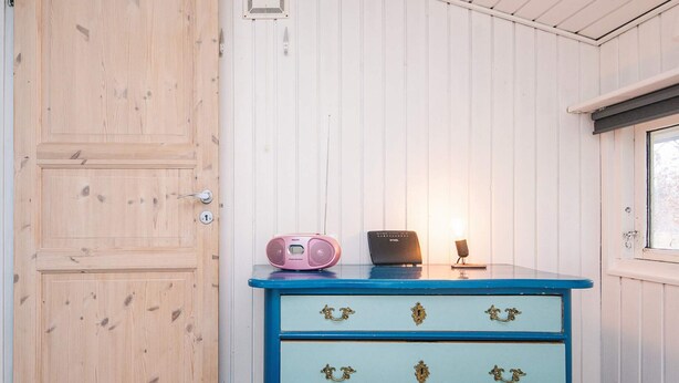 A room with a wooden door, a blue dresser with gold handles, a pink Philips radio, a black radio, and a small lamp. - 8 Person Holiday Home in Orsted (Ørsted)