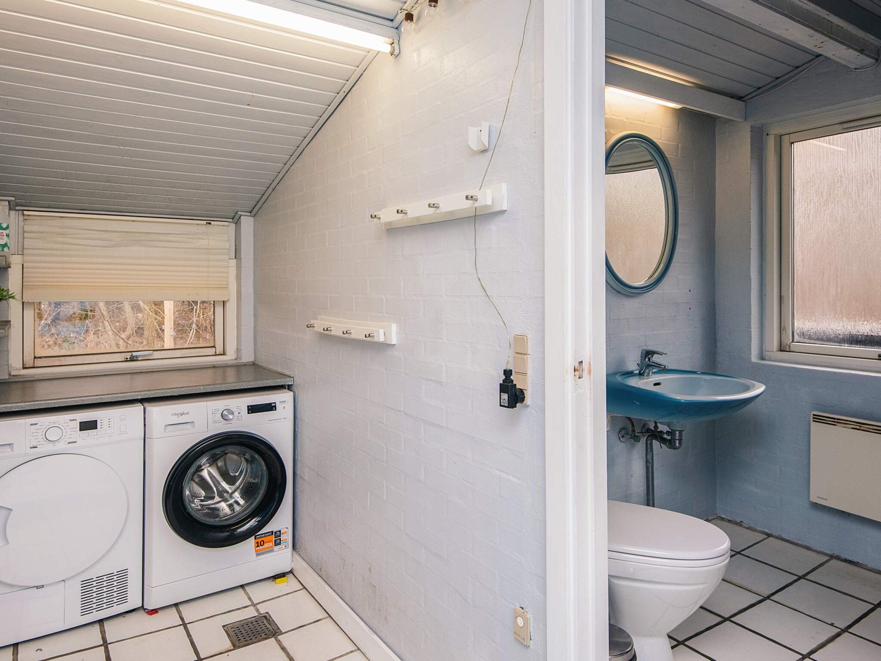 A compact bathroom with a washing machine, a toilet, a sink, and a window.