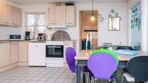 Eine kleine Küche mit Mikrowelle, Kaffeemaschine und Backofen. Ein Esstisch mit violetten Stühlen und einer Kerze.