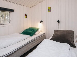 A room with two beds, one with a green pillow and the other with a brown pillow. There are two wall-mounted lamps.