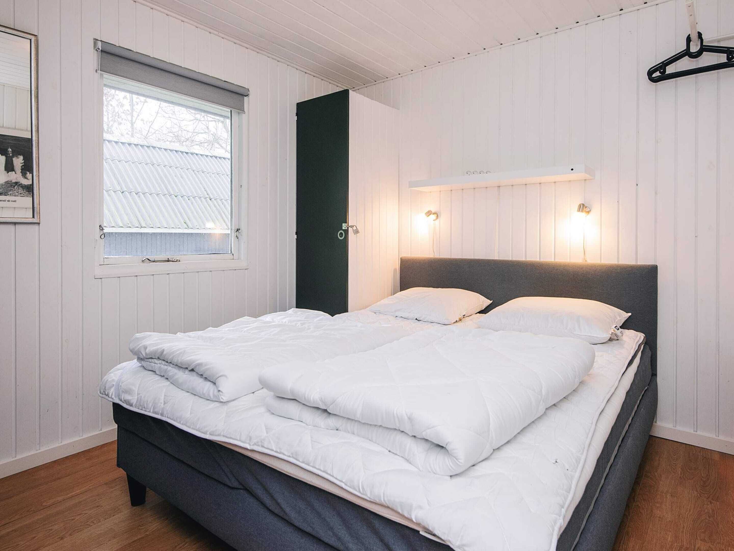 A bedroom with a bed, a window, a door, and a wall-mounted light fixture.