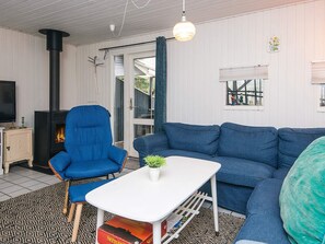 A living room with a blue sofa, a blue armchair, a white coffee table, a television, and a fireplace. - 8 Person Holiday Home in Orsted (Ørsted)