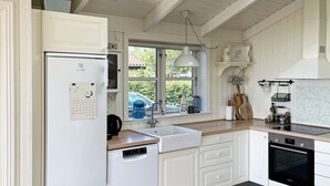 A modern kitchen with white cabinetry, a built-in dishwasher, a stove, and a window overlooking a car and greenery. - 8 Person Holiday Home in Broager-by Traum (Broager)