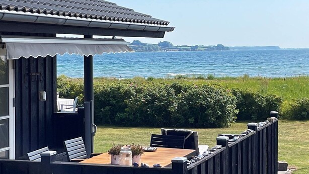 A wooden deck with a table and chairs, overlooking a body of water. - 8 Person Holiday Home in Broager-by Traum (Broager)