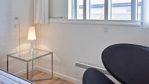 A room with a glass table, a lamp, a chair, and a window with a view of a building.