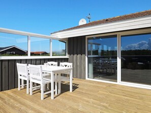 A wooden deck with a white table and chairs, large sliding glass doors, and a satellite dish on the roof. - Spacious Holiday Home in Jutland With Sauna (Lokken)