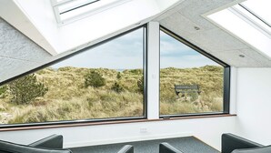 A modern room with large windows, black leather chairs, and a view of a grassy landscape. - 5 Star Holiday Home in Albaek (Aalbaek)