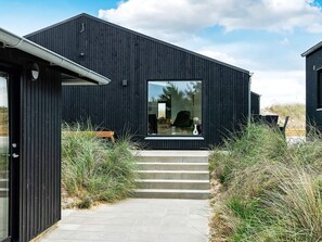 A modern building with a dark exterior, a large window, and a set of steps leading to the entrance.
