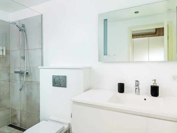 A modern bathroom with a shower, a toilet, a sink, and a mirror.