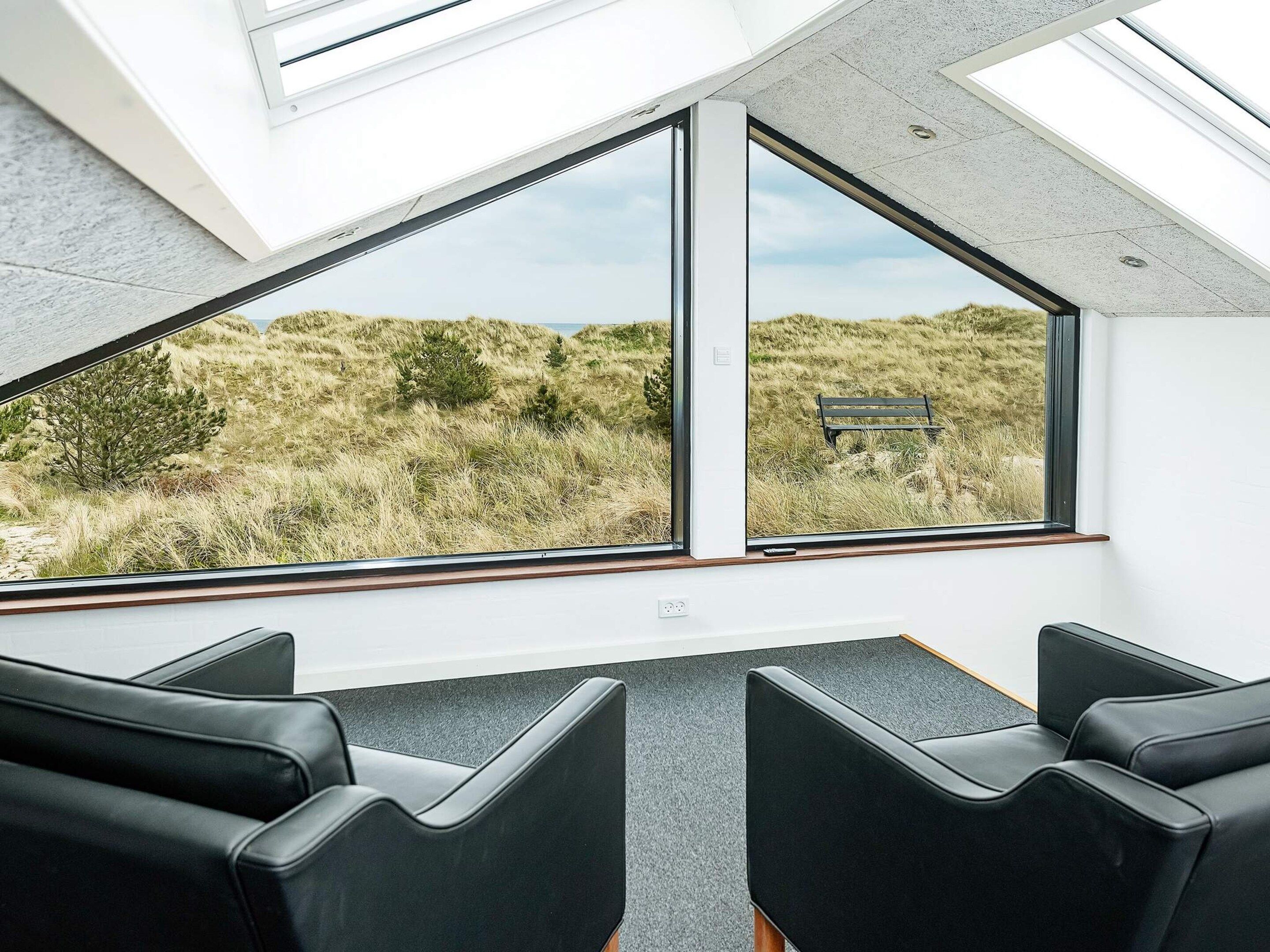 A room with two large windows offering a view of a grassy landscape and a bench. There are three black chairs in the room.