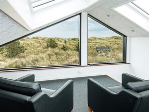 A room with two large windows offering a view of a grassy landscape and a bench. There are three black chairs in the room.