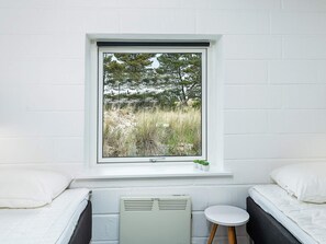 A room with a bed, a small table, a radiator, and a window with a view of trees and grass.