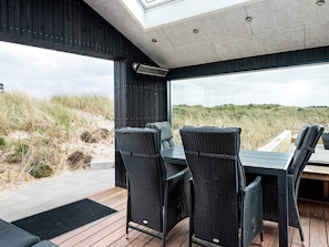 A modern outdoor dining area with wicker chairs and a table, overlooking a beach with dunes. - 5 Star Holiday Home in Albaek (Aalbaek)